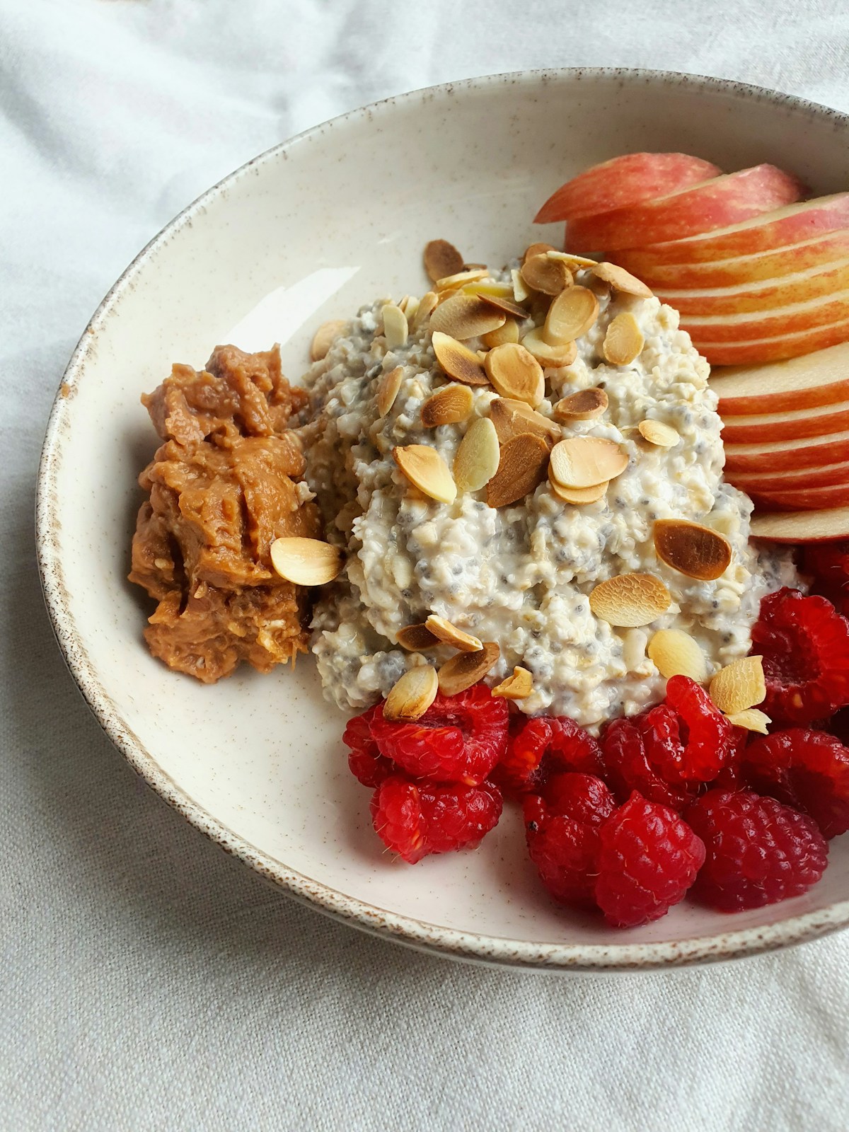Bowl de avena con frutos secos, frambuesas y manzana sobre fondo neutro